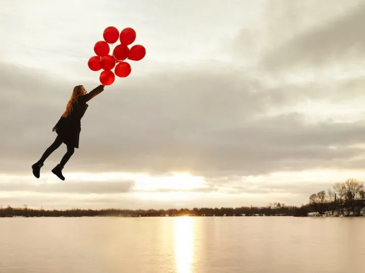 Imagination, happy girl fly with red balloons at sunset on the frozen river, follow your dream