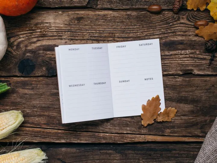 white notebook planner, pumpkins and corn with yellow leaves on a wooden background