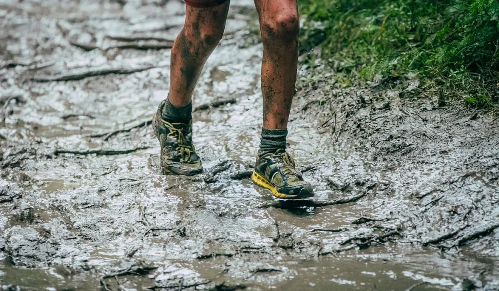 crop photo lower part of an athlete running on mud 