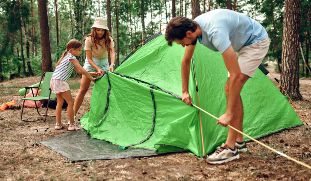 Family on vacation in the forest setting up green tent