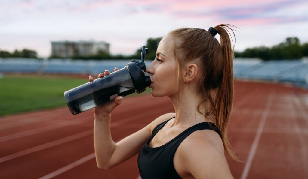 Female runner drinks water on training stadium