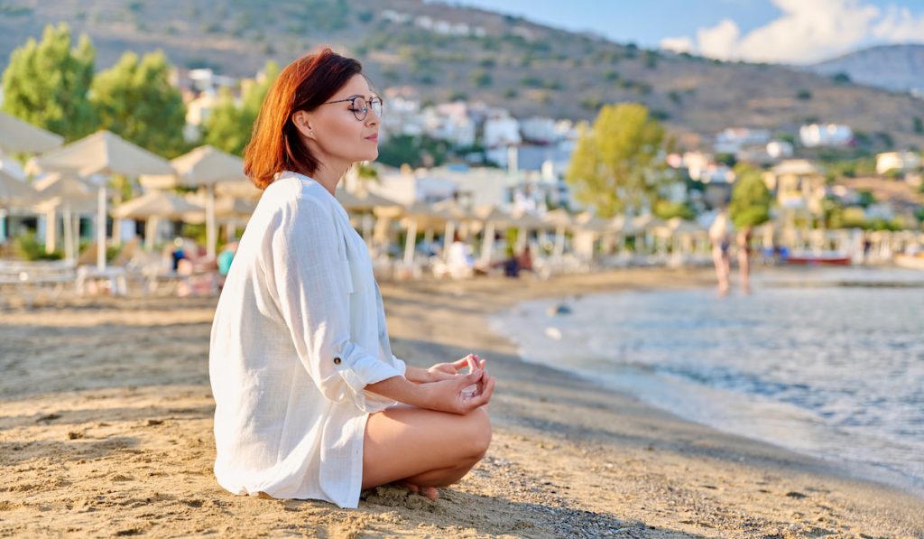 Mature woman sitting in lotus position meditating on the beach