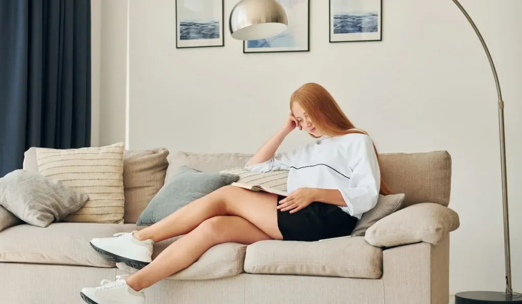 Reading book. Female teenager with blonde hair is at home at daytime