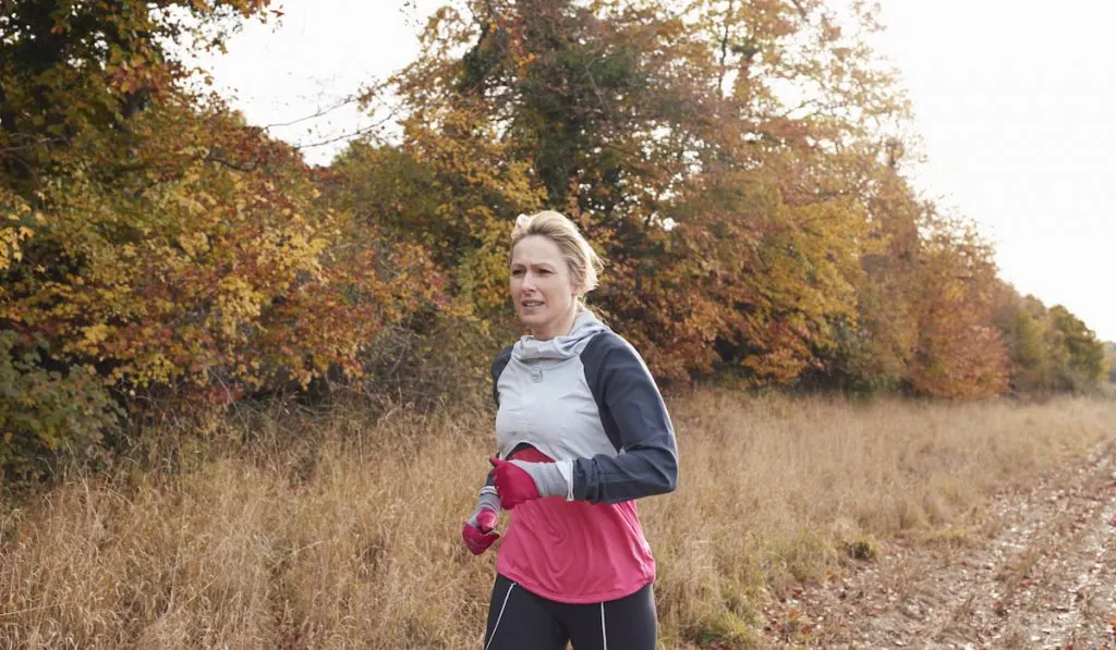 woman running around muddy road with gloves 