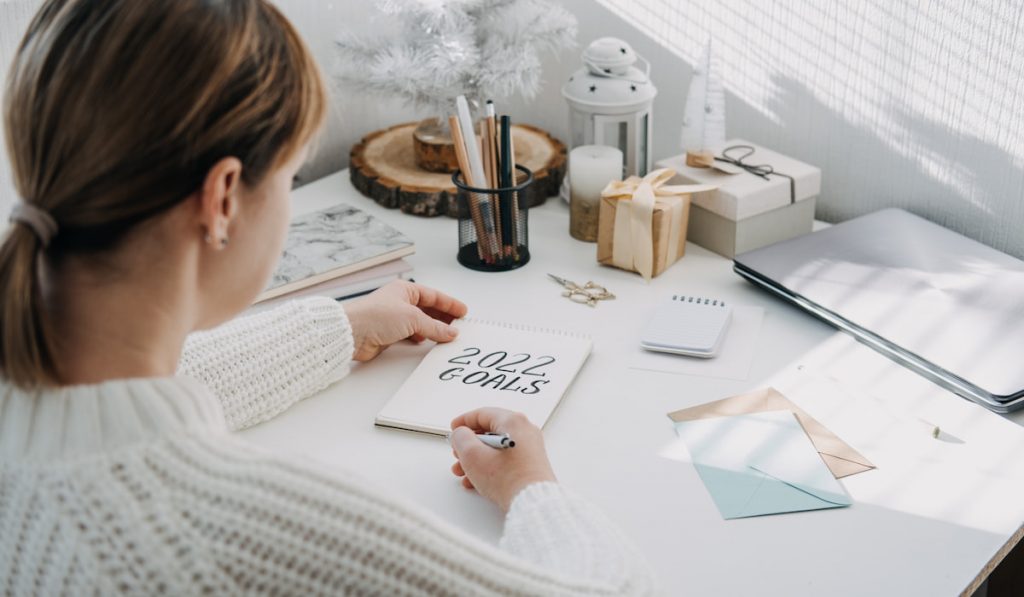 Woman in white sweater writing Text 2022 goals