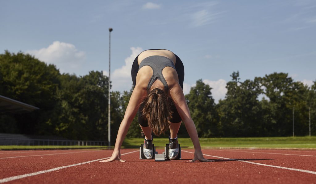 Young female runner bending forward on race track starting line