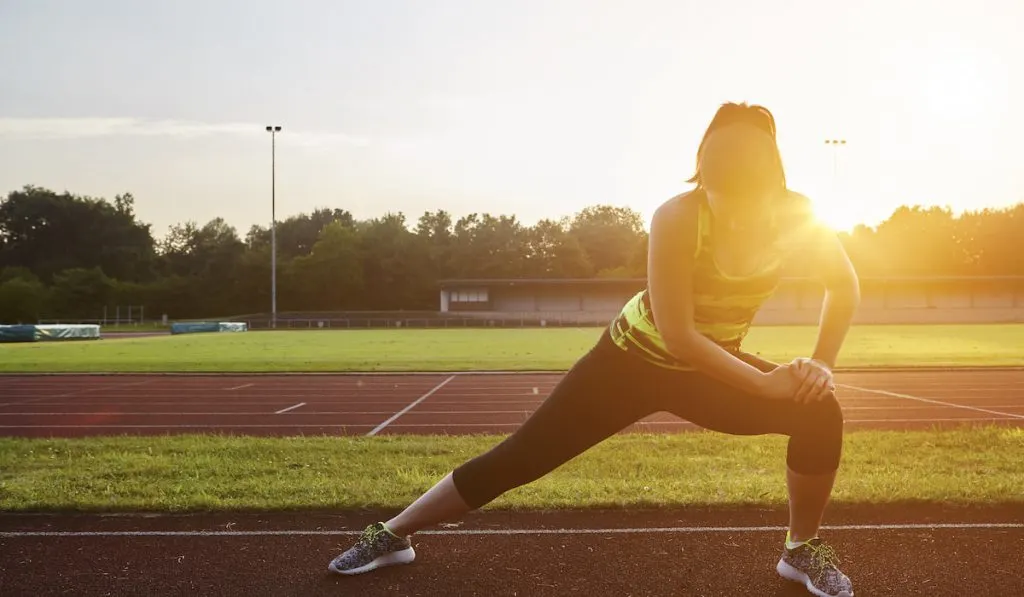 Young female runner stretching on sunlit race track