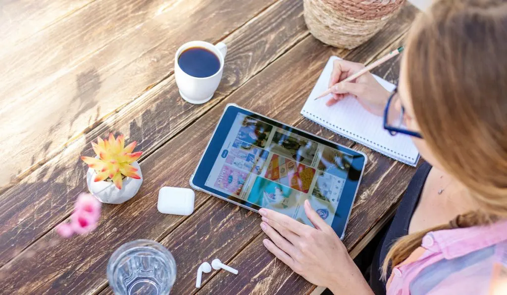 Young lady searching inspiration from Pinterest app ad writing notes