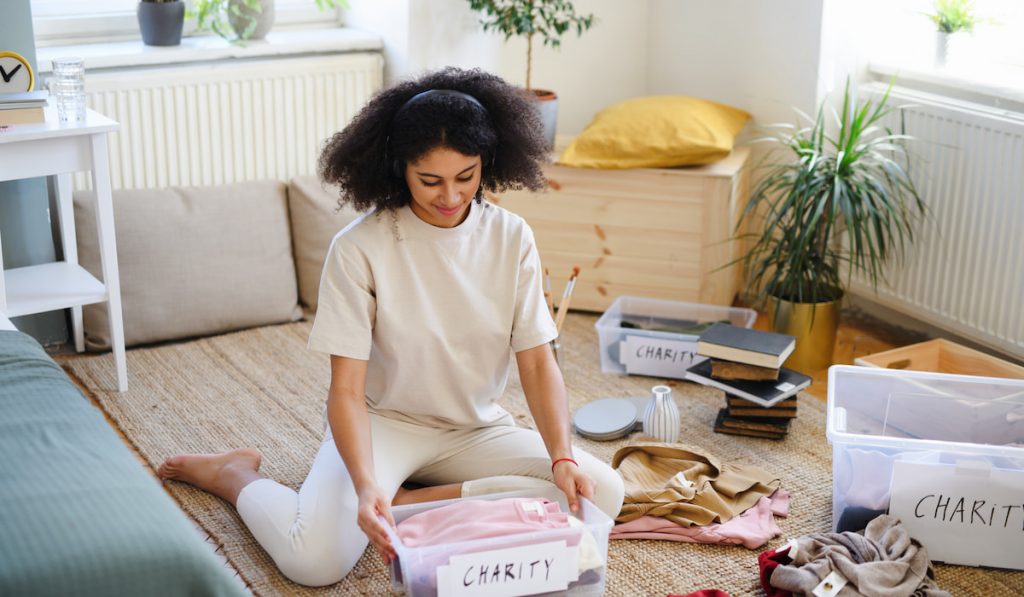 Young woman decluttering wardrobe indoors at home, charity donation concept.