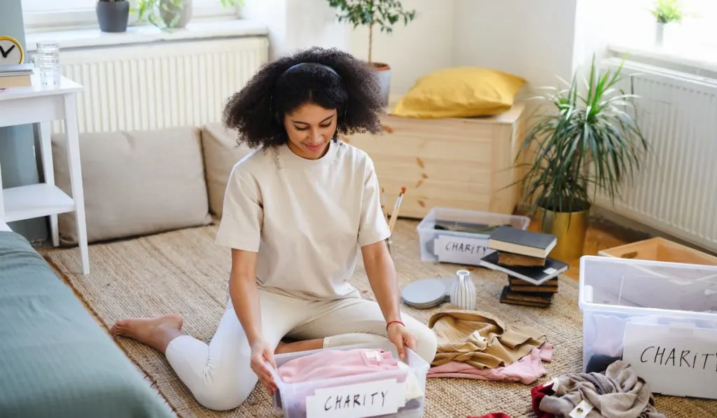 Young woman decluttering wardrobe indoors at home, charity donation concept.