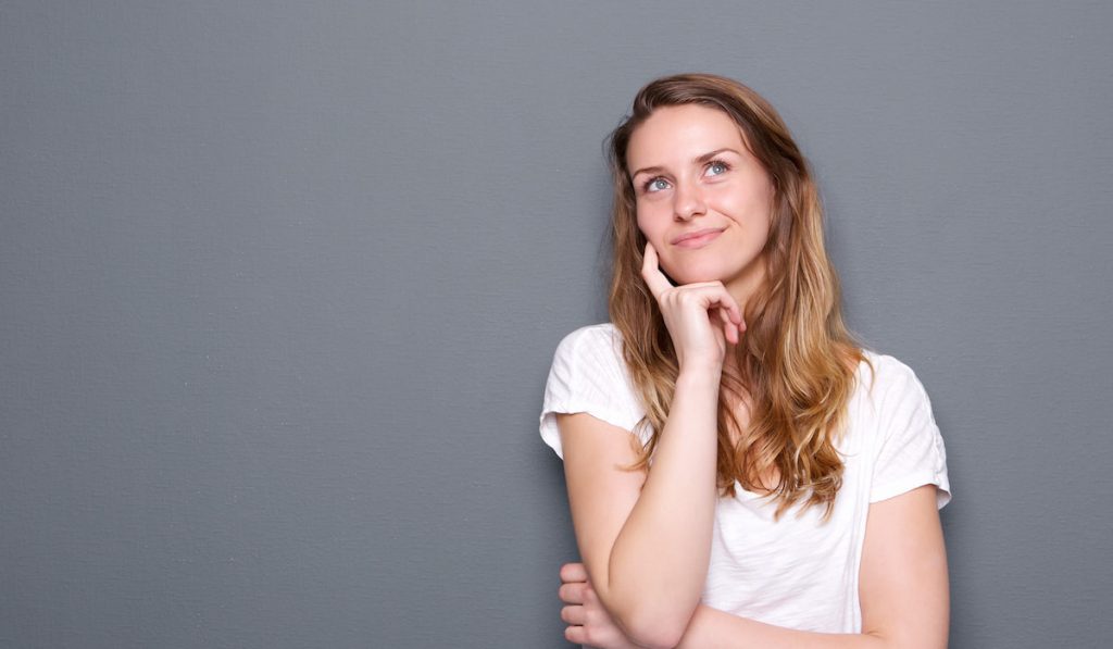 Young woman thinking on gray background