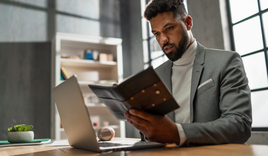 a businessman with diary working on laptop indoors in office