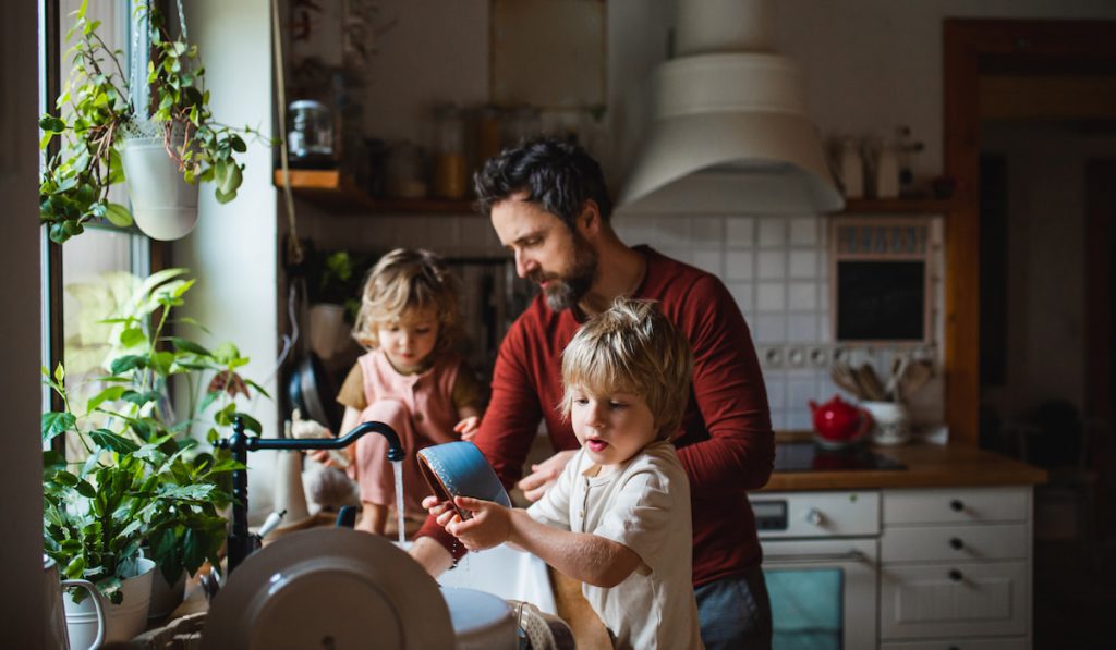 father with two small children washing dishes indoors at home