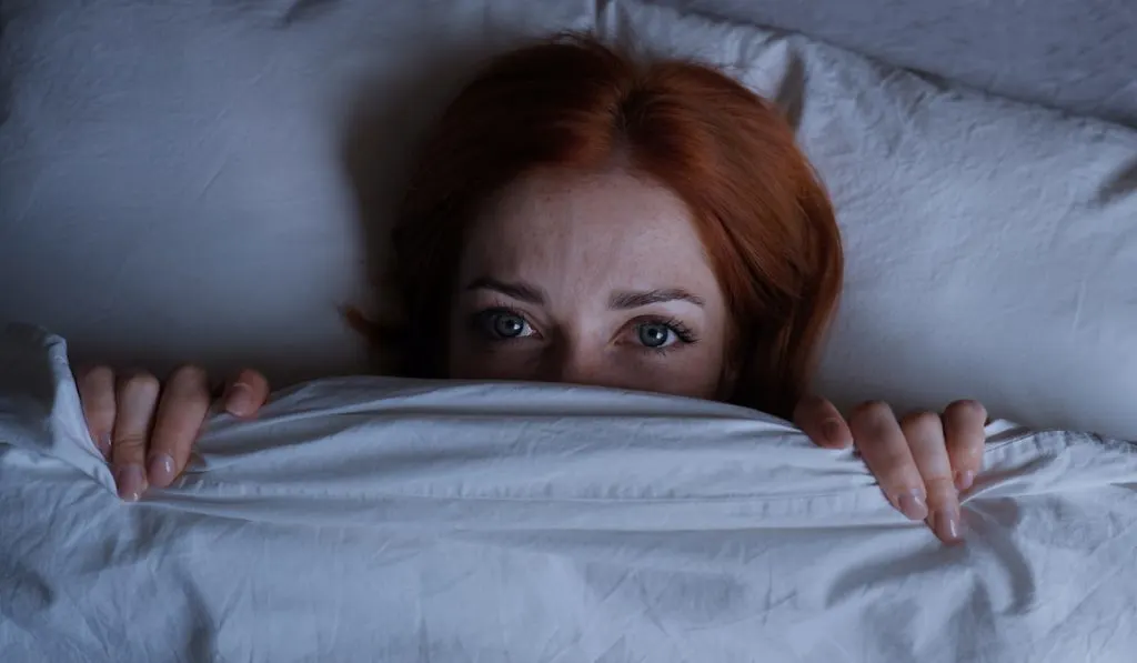 scared woman lying in bed because of her nightmare