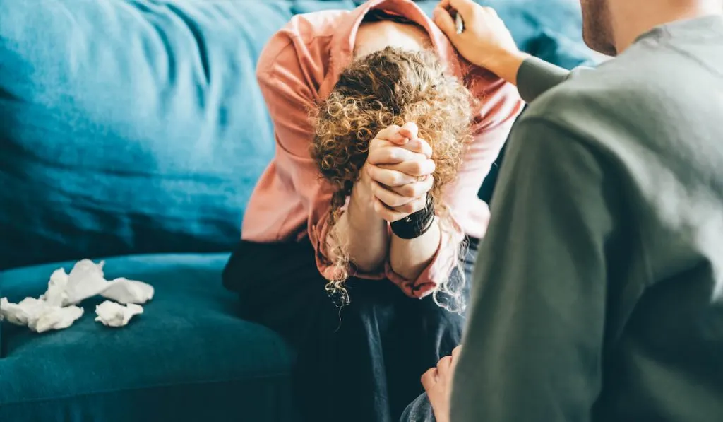 woman cries and sitting on blue sofa at appointment with professional psychologist