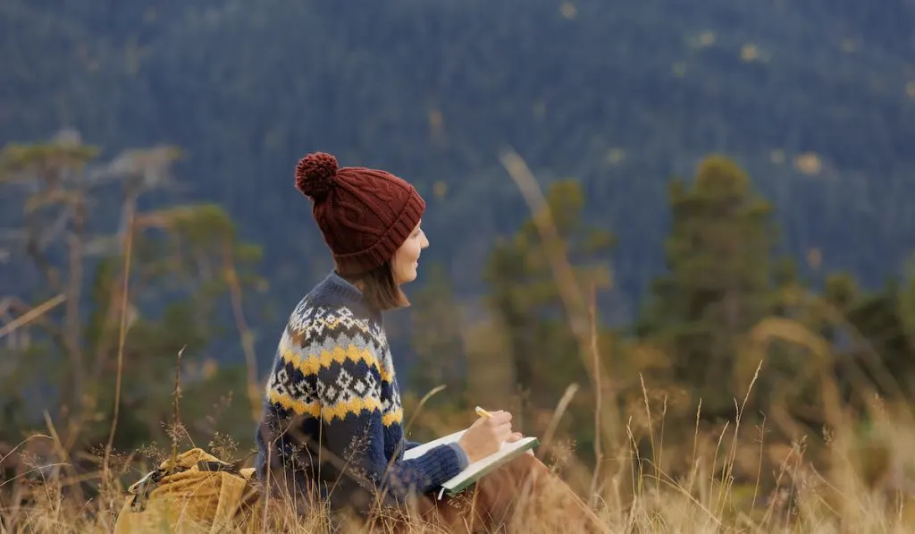 woman in the mountain resting and writing about herself in her notebook