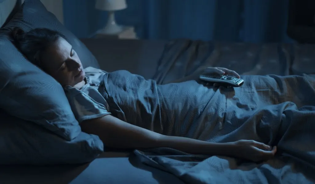 woman sleeping on her bed while holding her TV remote 