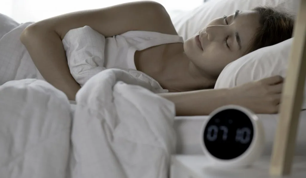 woman sleeping on her bed with clock on her side