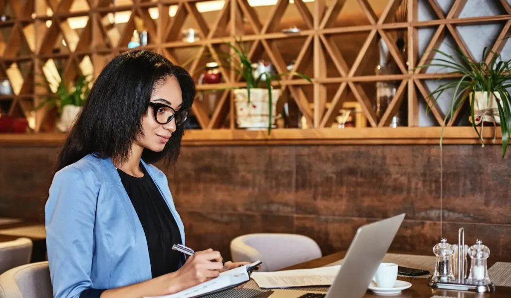 woman viewing goal list on a laptop while writing on a notebook