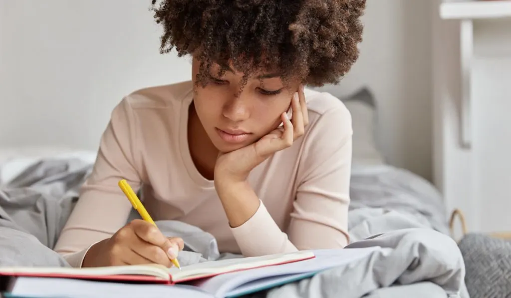 woman writing down her dream in notebook while on her bed