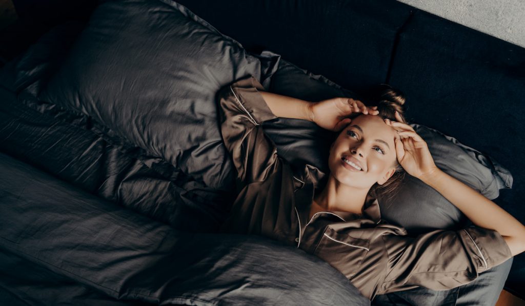 young girl in satin pajama thinking while lying in bed 