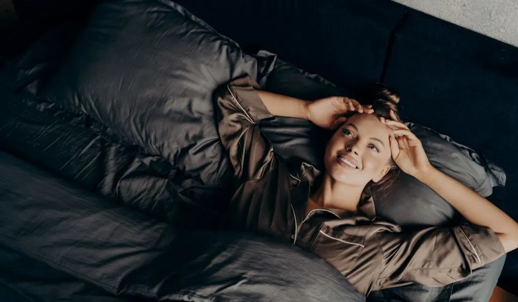 young girl in satin pajama thinking while lying in bed