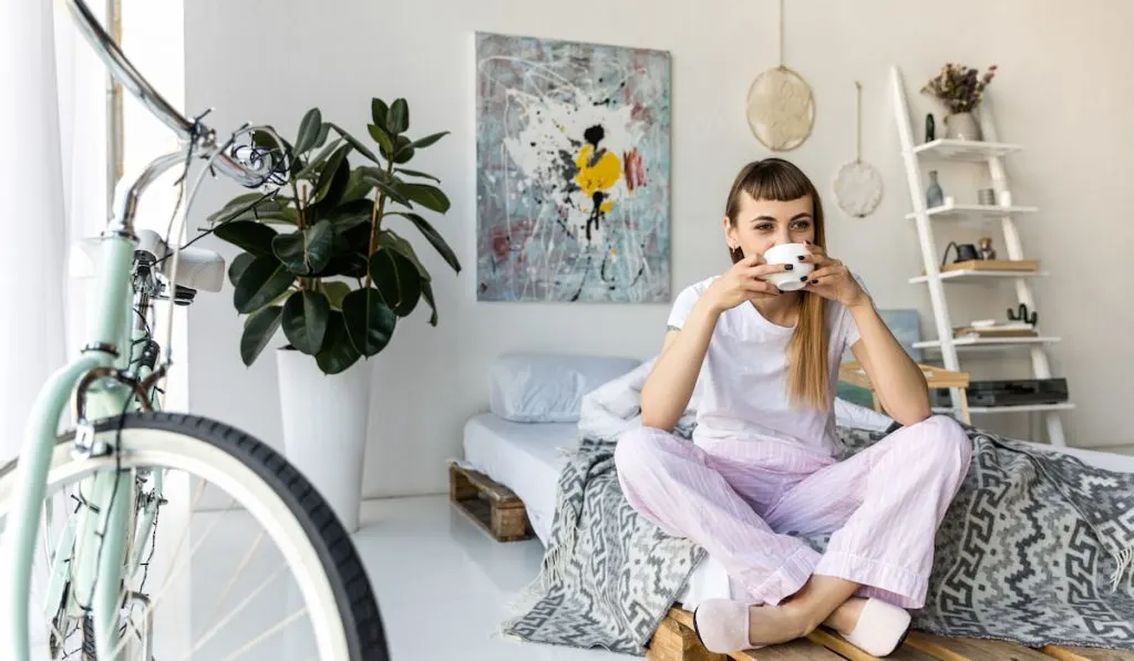 young woman drinking coffee while resting on bed in morning at home