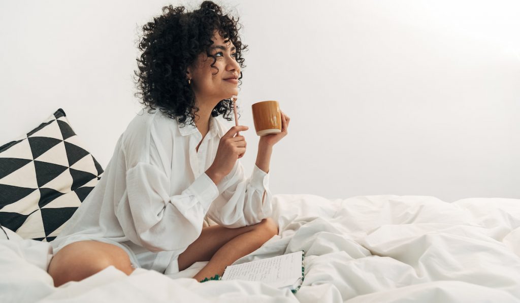 young woman having a coffee in bed and writing on her journal -