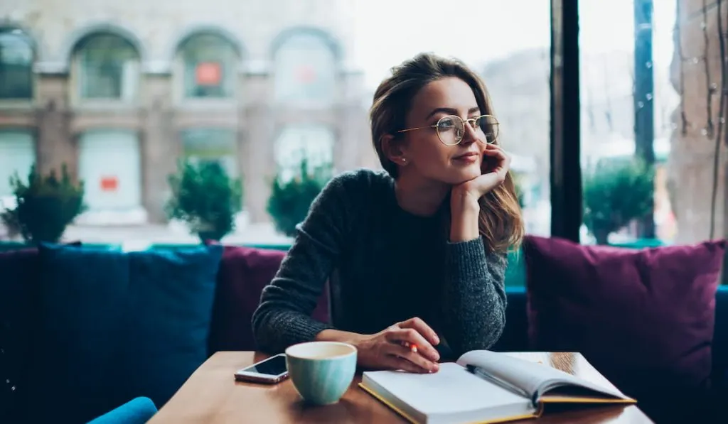 attractive young woman in eyeglasses writing in her notebook
