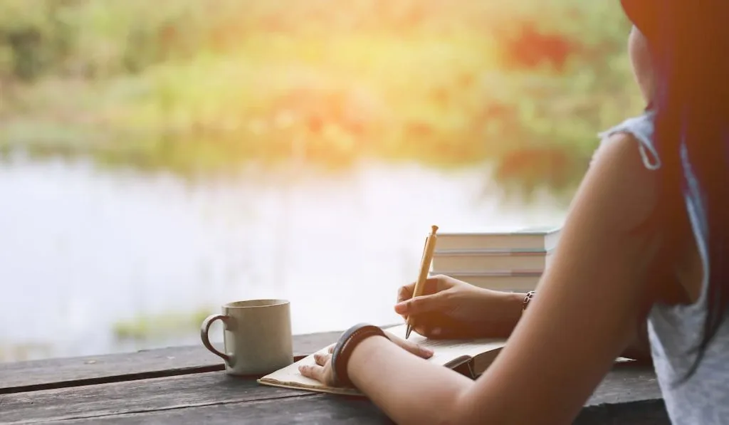 woman writing on notebook with coffee cup on green background